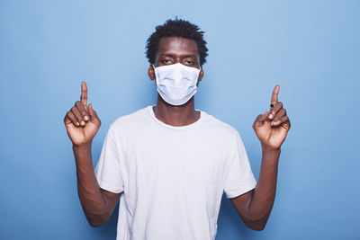 Portrait of young man holding mask against blue background