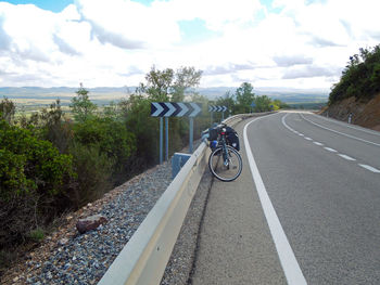 Bicycle parked on road against cloudy sky