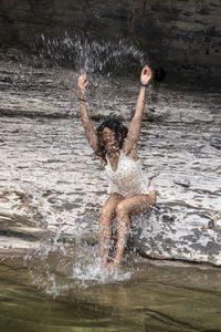 Brunette woman sitting on the shore of a mountain lake splashing herself