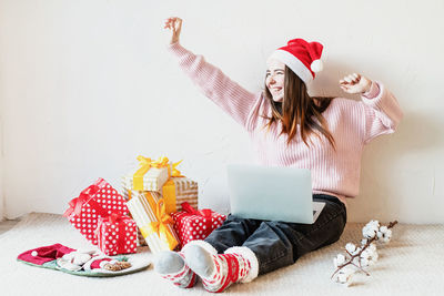 Smiling young woman with laptop while sitting by christmas gift at home