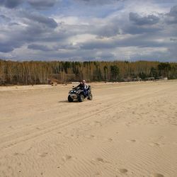 Man riding motorcycle on desert against sky