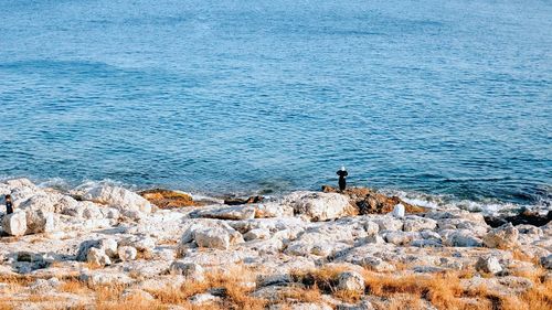 Man standing on rock by sea against sky