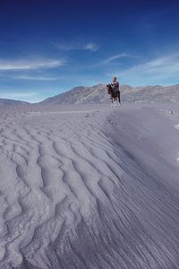 Man riding horse on desert against sky