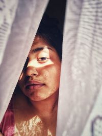 Close-up portrait of woman seen through curtain at home