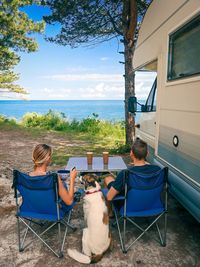A young couple a d dog eating in front of the motorhome. sea view