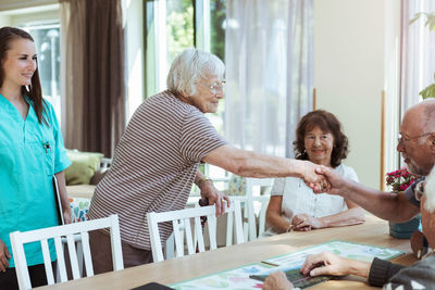 Nurse looking at senior woman greeting friends at nursing home