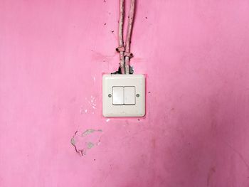 Close-up of white electric switch on pink wall