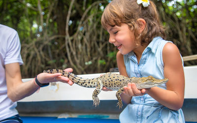 Smiling girl holding alligator by man