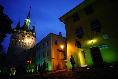 People on illuminated street amidst buildings at night