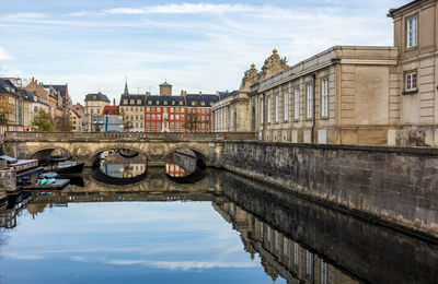 Arch bridge over river by buildings against sky