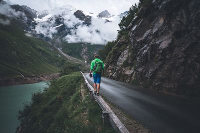 Rear view of male hiker with backpack walking on railing by road