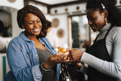 Happy female hairdresser discussing with coworker on beauty product in barber shop