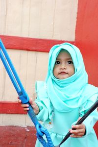 Smiling cute girl in hijab standing against wall outdoors