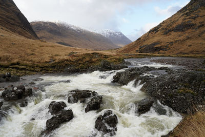 Scenic view of river flowing through mountains against sky