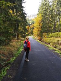 Rear view of woman walking on road in forest