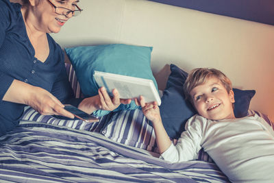 Grandmother giving book to grandson on bed at home