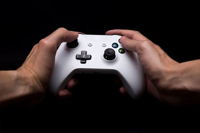 Cropped hands holding game controller against black background