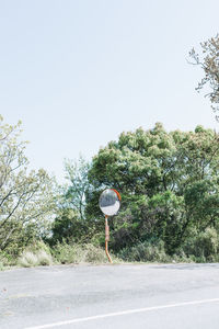 Road sign by trees against clear sky