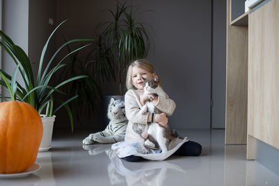 A little girl sits on the floor and holds a cat in her hands