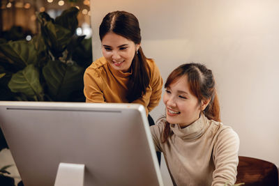 Smiling young woman using phone while sitting on laptop