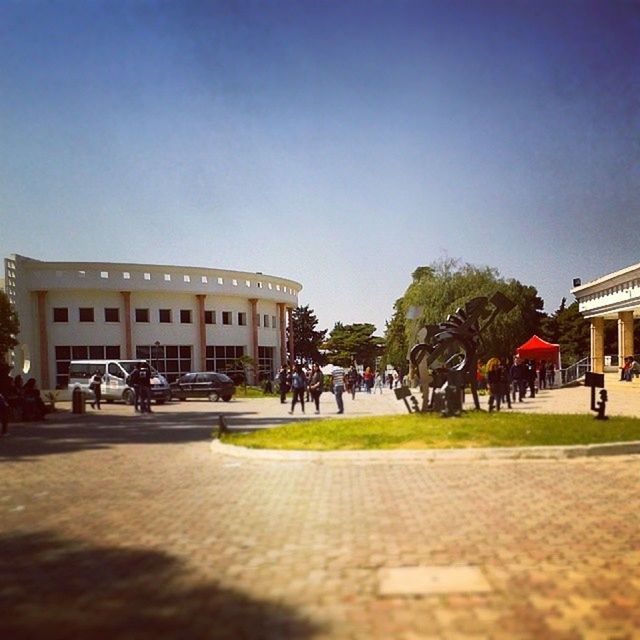 building exterior, architecture, clear sky, built structure, copy space, tree, incidental people, street, grass, travel destinations, city, road, outdoors, history, large group of people, facade, lawn, person, day