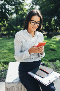 Happy businesswoman using smart phone on sunny day