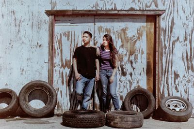 Friends standing amidst tires against wall