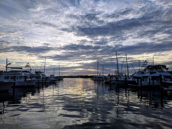 Sailboats moored in harbor at sunset