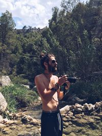 Young man holding camera while standing against mountain