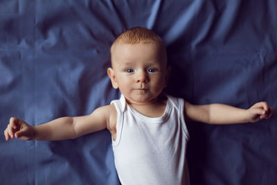 Baby boy blonde in white bodysuit lying on the bed