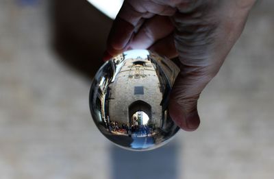 Cropped hand holding crystal ball building reflection