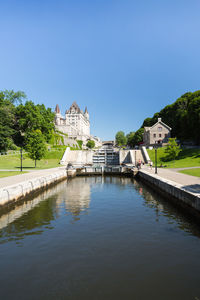 View of building by lake against clear blue sky