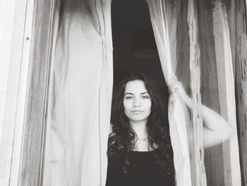 Portrait of young woman standing against curtain at home