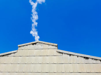 Low angle view of smoke emitting from building against clear blue sky