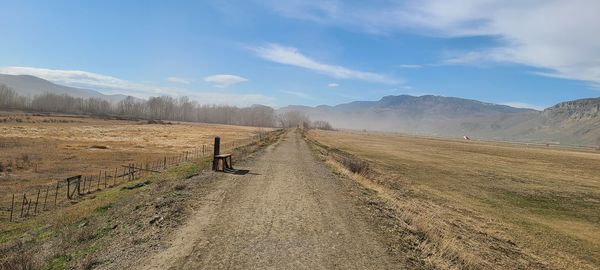 Empty road amidst field against sky