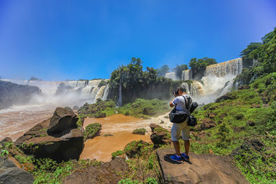 Rear view of man photographing on rock against sky