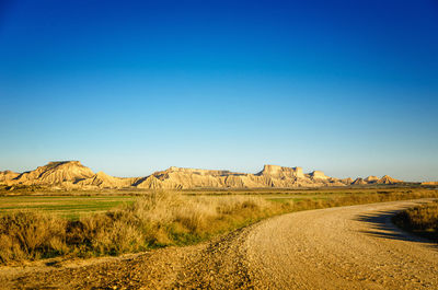Scenic view of road amidst field against clear blue sky, bardenas reales, spain