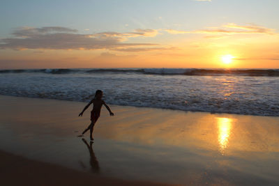 Boy running at beach against sky during sunset