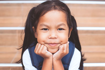 Close-up portrait of cute smiling girl with hands on chin