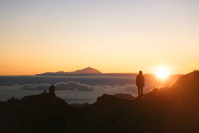 Silhouette of young woman between big rocks during sunset in gran canaria with teide