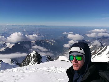 Young man standing on snowcapped mountain against sky during winter