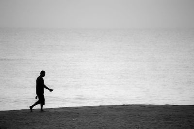 Silhouette man walking on beach against sky