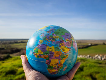 Cropped hand holding globe against blue sky