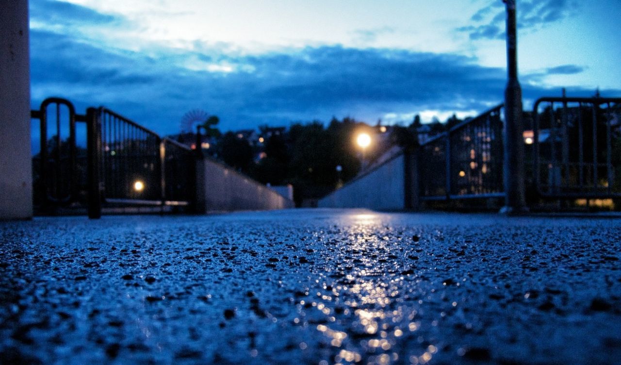 surface level, illuminated, building exterior, sky, street light, architecture, the way forward, street, night, built structure, road, city, lighting equipment, dusk, empty, diminishing perspective, asphalt, weather, wet, cloud - sky