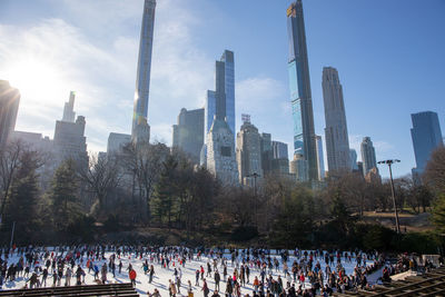 People by modern buildings in city against sky