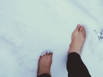 Low section of mature woman standing on snow covered field