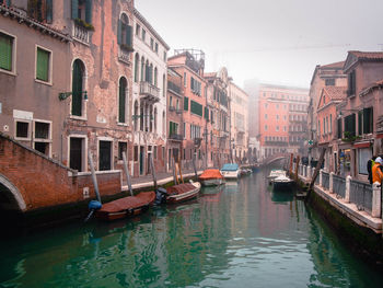 Boats moored in canal amidst buildings in city against sky