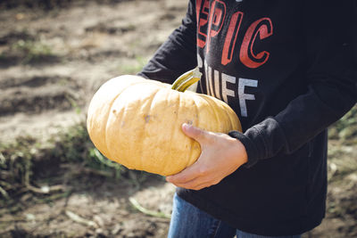 Midsection of man holding pumpkin while standing on field