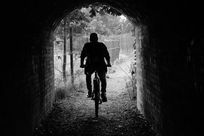 Rear view of man riding bicycle in tunnel