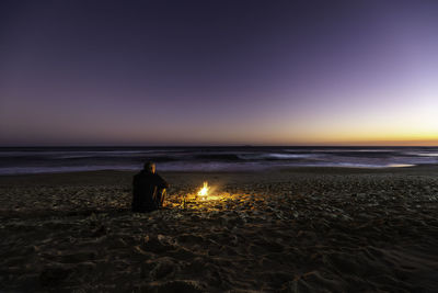 Rear view of a lonely guy and bonfire on the beach at sunset